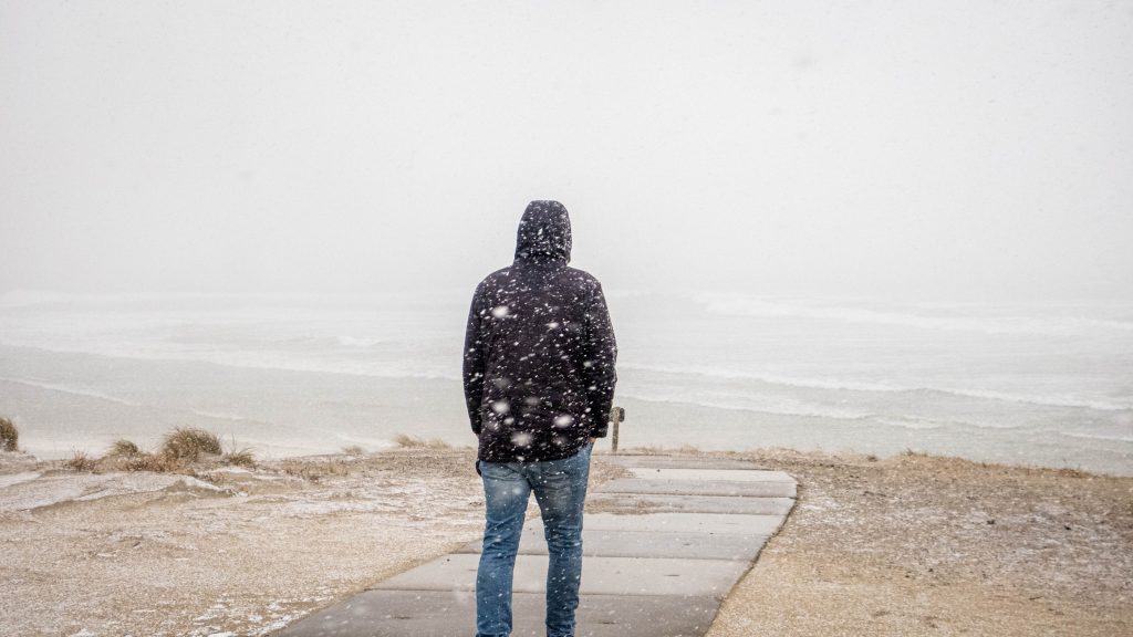 a man standing on the beach in the middle of a snow storm