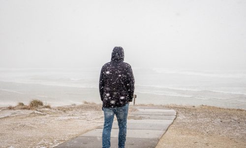 a man standing on the beach in the middle of a snow storm